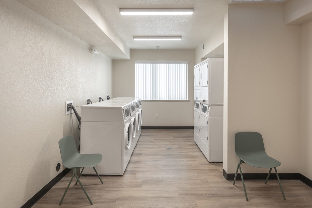 A laundry room with a washer and dryer, two chairs, and a window.
