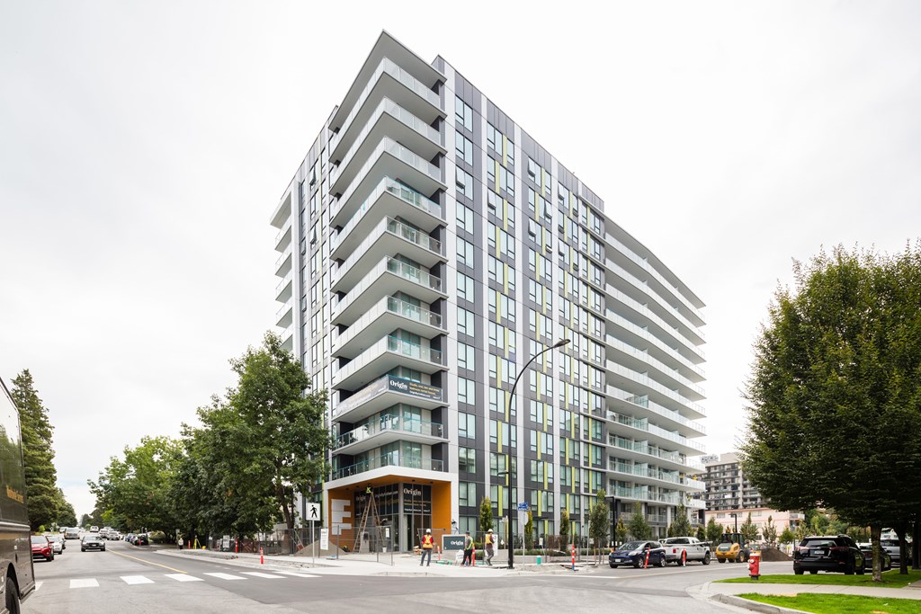 A modern multi-story building with a glass facade is situated on a street corner.