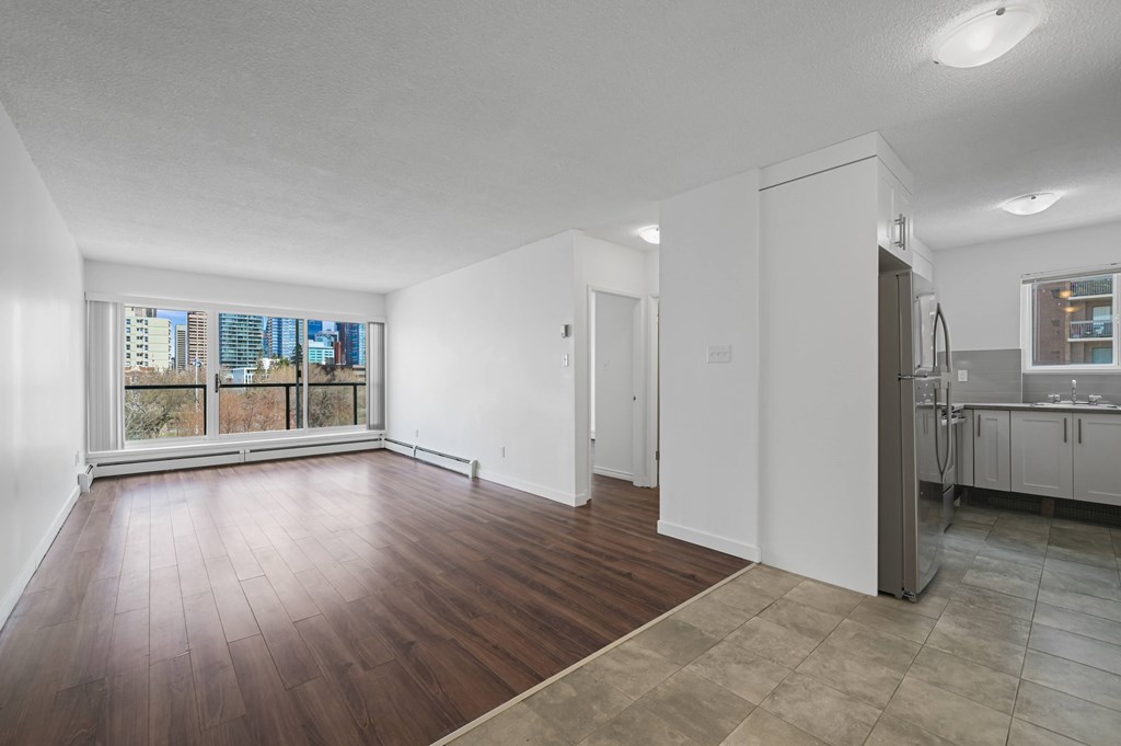 A large empty room with wooden floors and a kitchen area to the right.