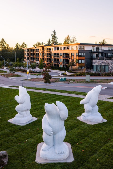 Four white bear statues are on a lawn in front of a building.