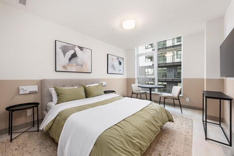 A bedroom with a large bed and a view of a building outside the window.