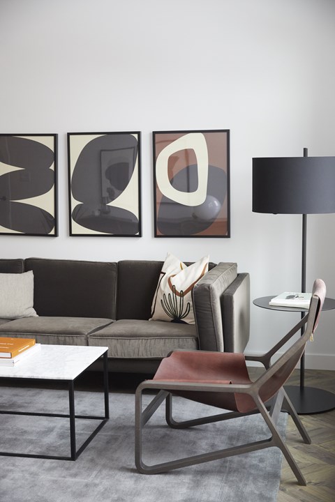A modern living room with a grey sofa, a coffee table, a chair, and three abstract paintings on the wall.