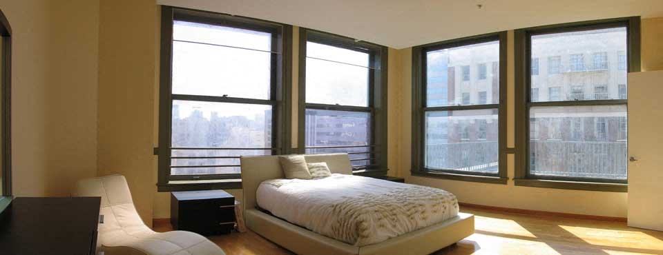 A bedroom with a bed, chair, and large windows.
