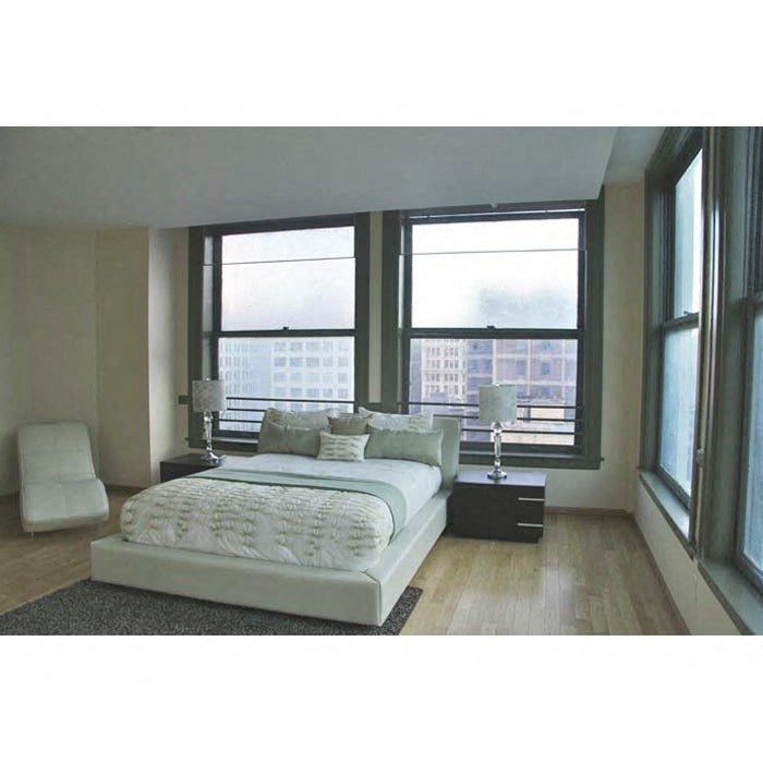 A bedroom with a large bed and a view of a cityscape through the windows.