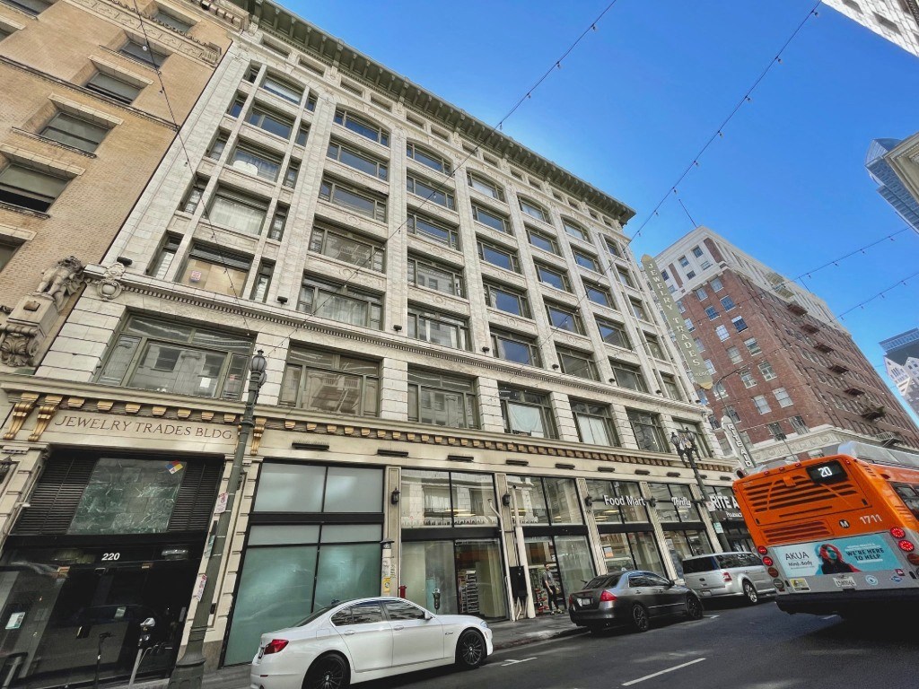A white car is parked in front of a building with a sign that says "Jewelry Trades Bldg.".
