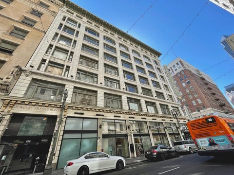 A white car is parked in front of a building with a sign that says "Jewelry Trades Bldg.".
