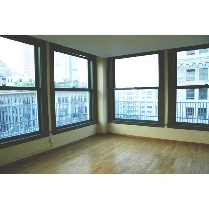 A room with wooden floors and three windows overlooking a city.