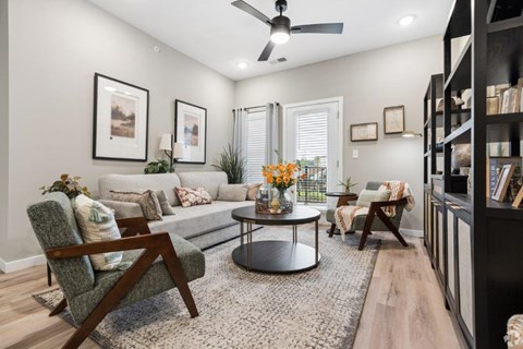 A living room with a grey sofa, a round coffee table, a wooden chair, and a ceiling fan.