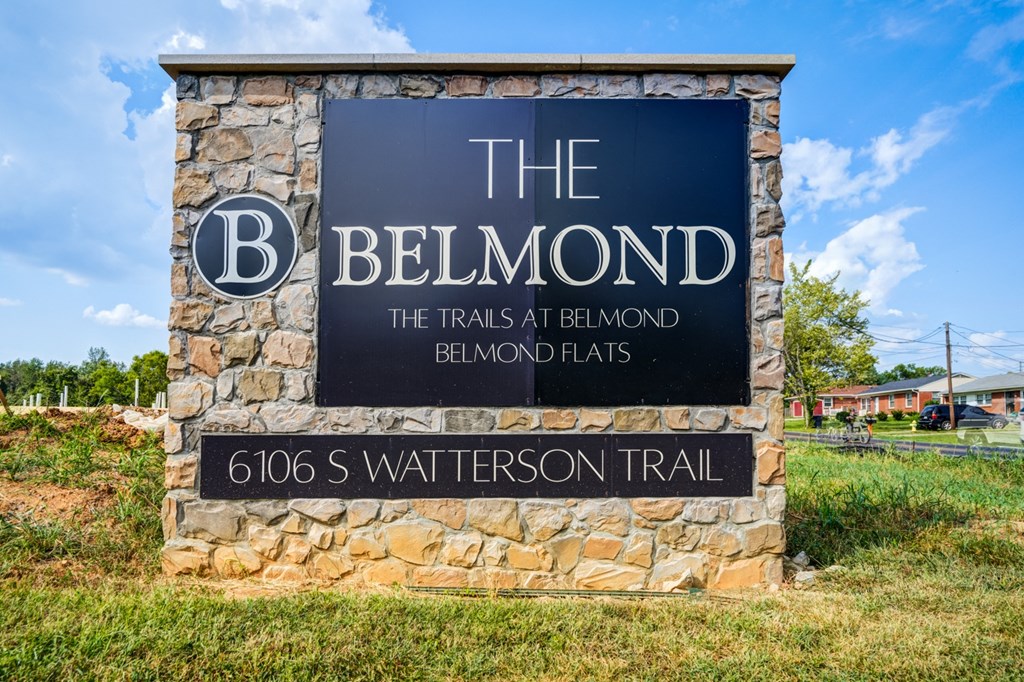 A sign for The Belmond Trails at Belmond Flats stands in front of a grassy area.