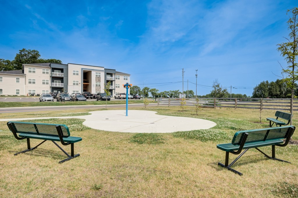 two park benches in a park with a pole and buildings