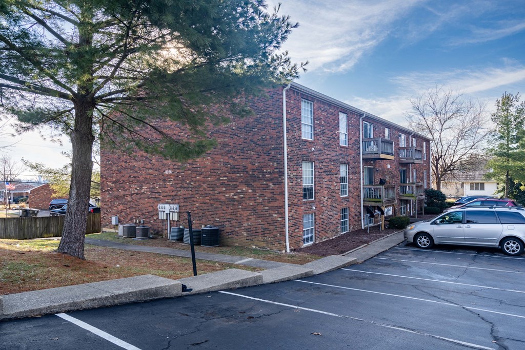 A parking lot in front of a brick building with a tree on the left.
