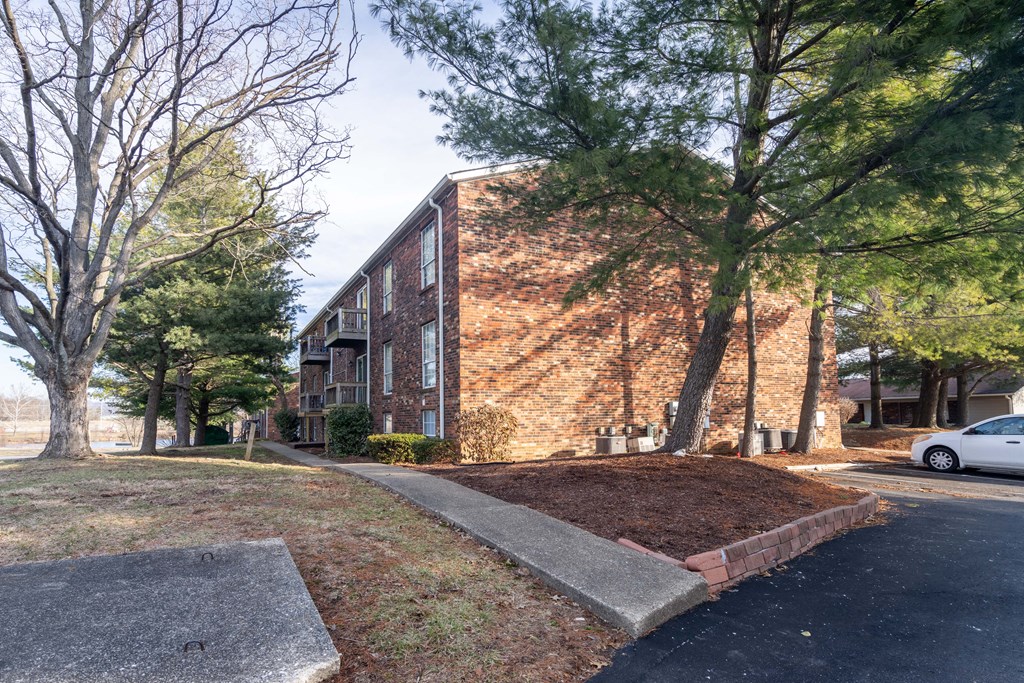 A white car is parked on the street in front of a brick building.