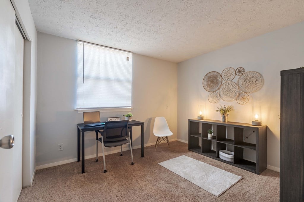 A room with a desk, chair, and shelves with decorative items.