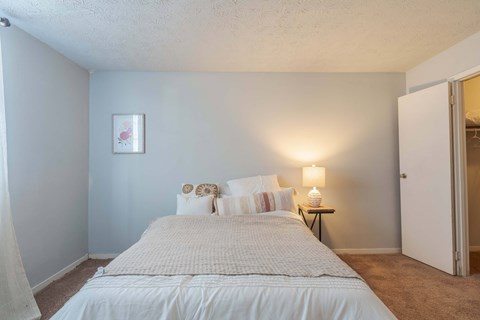 A bedroom with a bed, pillows, a nightstand, and a lamp.