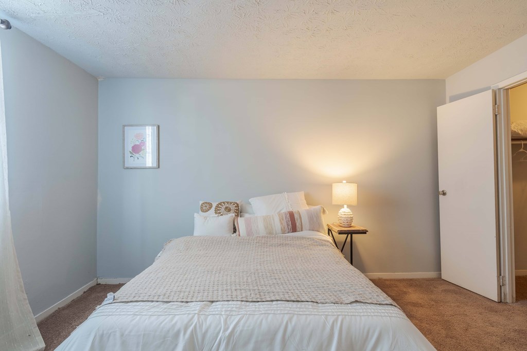 A bedroom with a bed, pillows, a nightstand, and a lamp.