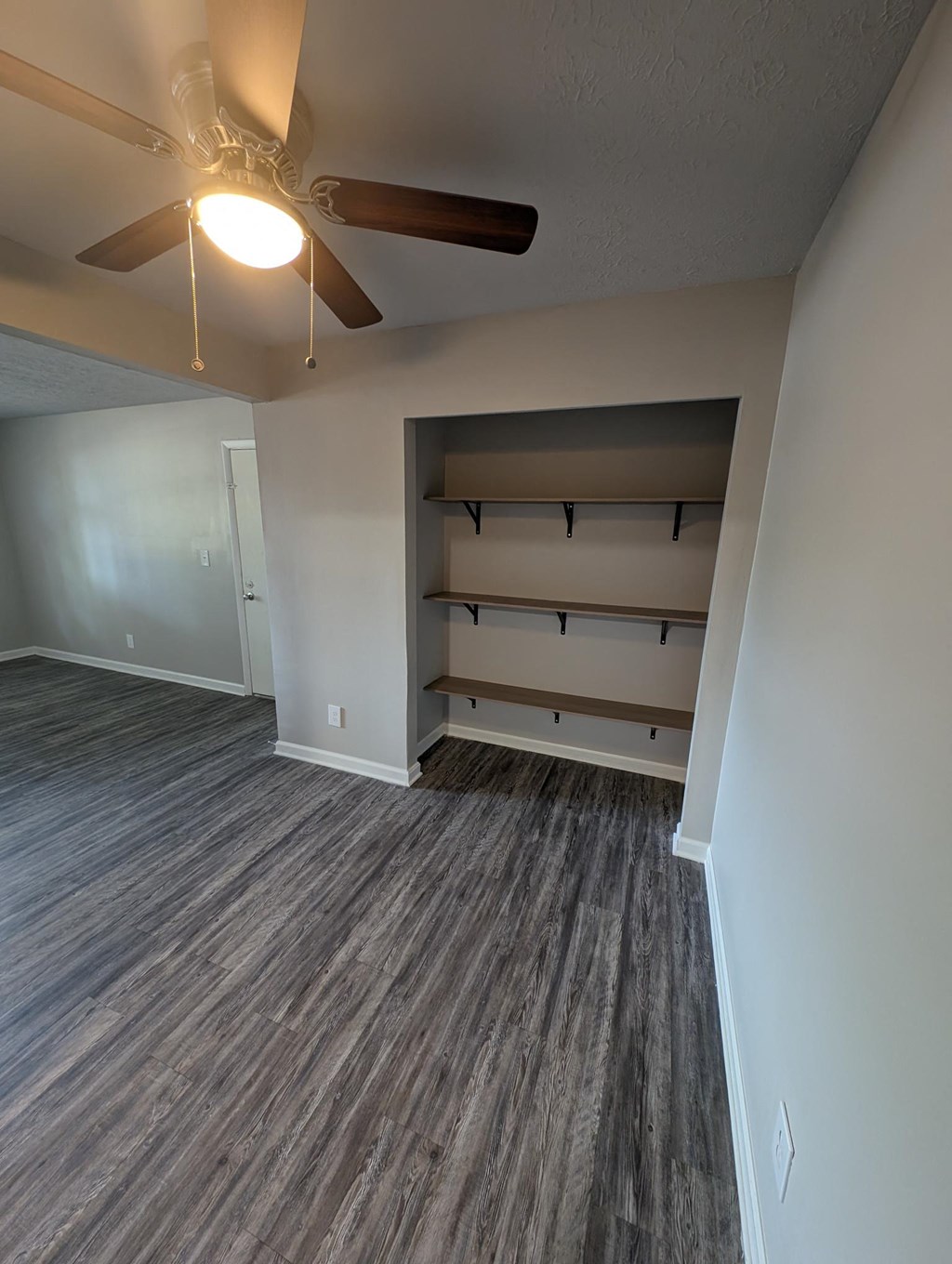 an empty living room with a ceiling fan and shelves