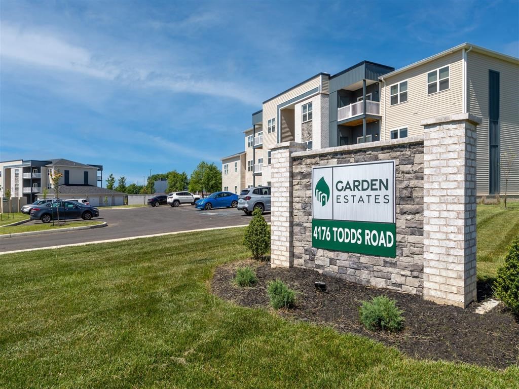 an apartment building with a sign for garden estates and a parking lot