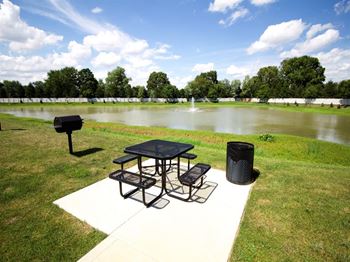 a picnic area with a table and a grill next to a pond