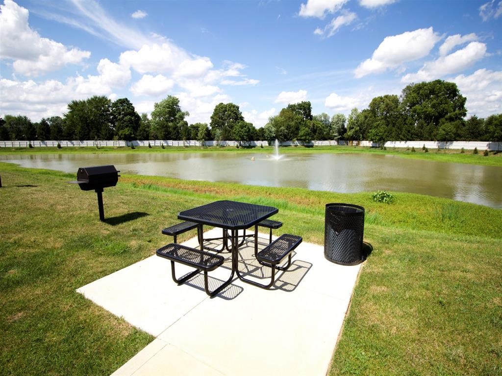 a picnic area with a table and a grill next to a pond
