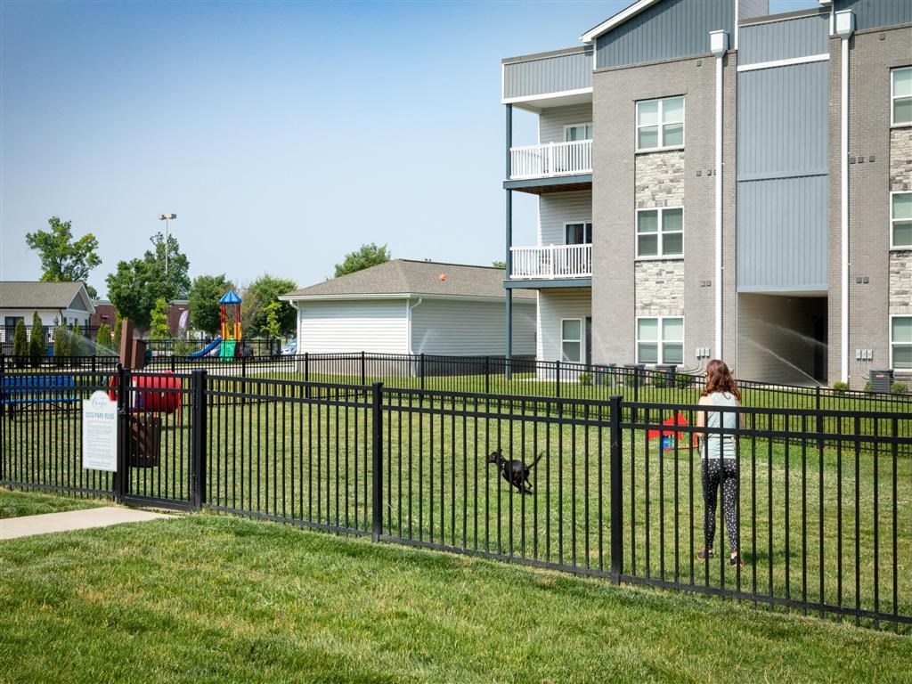 a girl is standing in a yard with a dog behind a fence