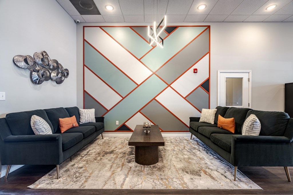 A living room with two black couches and a coffee table in front of a wall with a red and white geometric design.