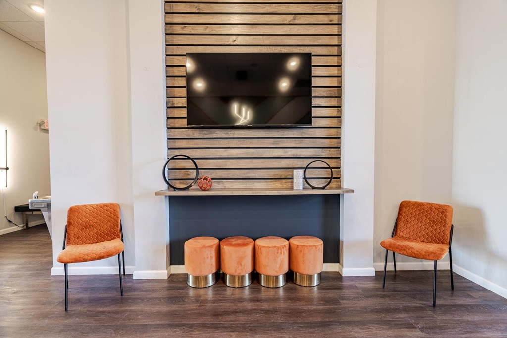 Two orange chairs are placed in front of a fireplace with a TV above it.