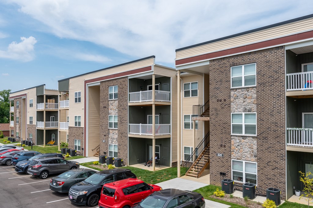an exterior view of an apartment building with cars parked in a parking lot