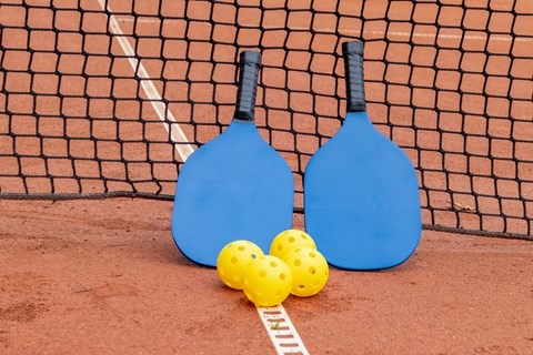 Two blue paddles and three yellow balls on a red surface.