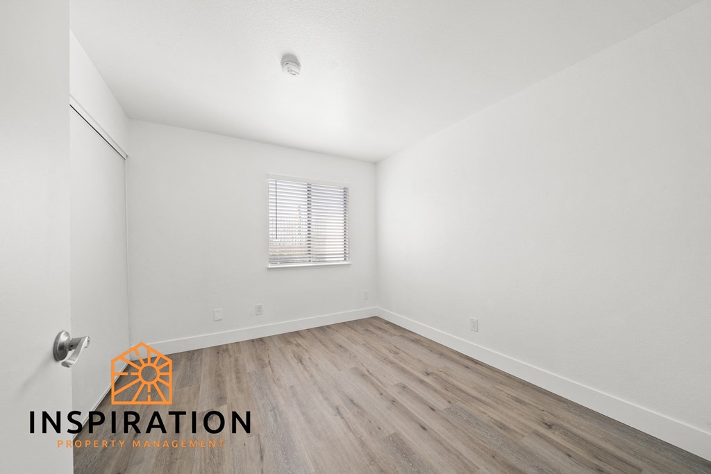 the living room of an apartment with white walls and wood floors