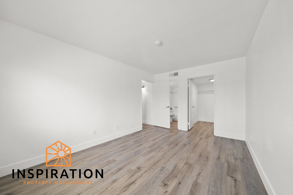 the living room and dining room of an apartment with white walls and wood flooring