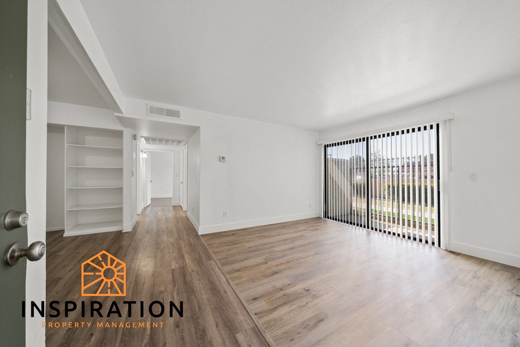 the living room and dining room of an apartment with wood floors and a large window
