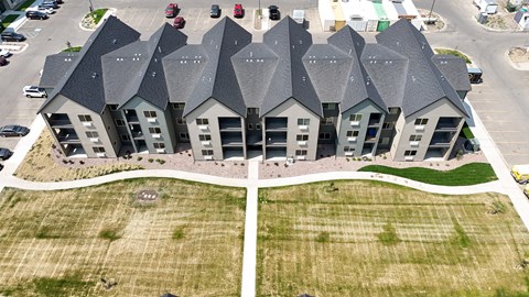 A large building with grey roofs and a parking lot in front.