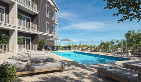 A large swimming pool is surrounded by a sun lounger and a building.