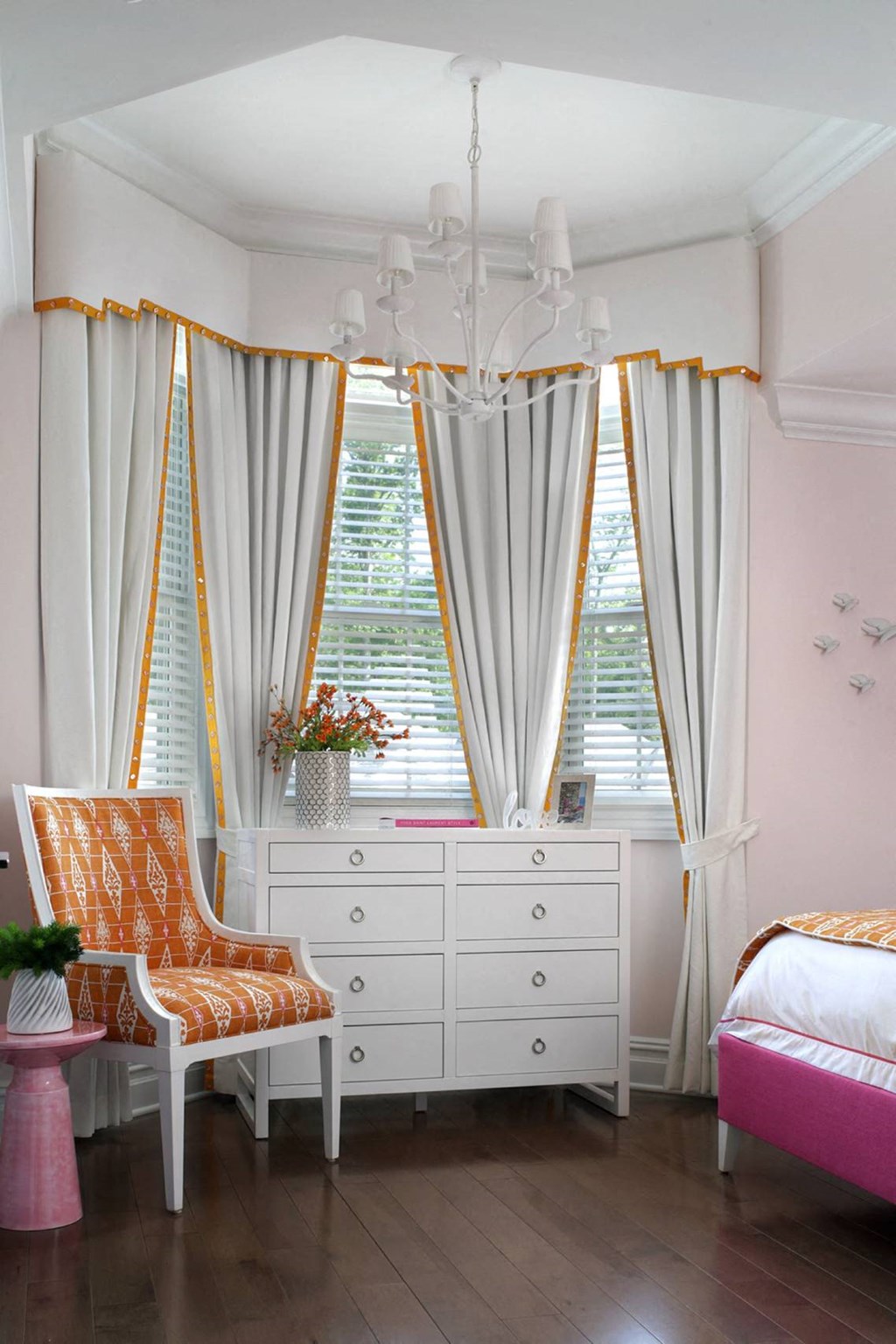 a bedroom with three windows with white curtains and a white dresser and a chair