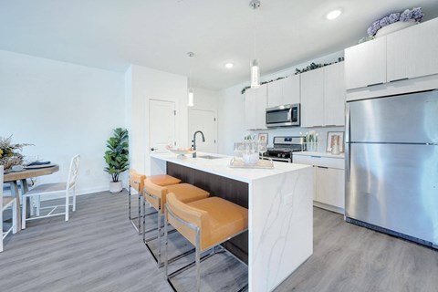 a kitchen with stainless steel appliances and a bar with orange stools at The Franklin at Hillsborough Apartments, New Jersey, 08844
