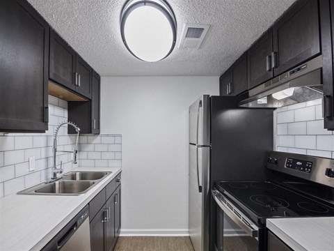 A kitchen with black cabinets and a stainless steel refrigerator.