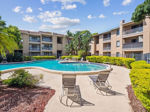 A pool surrounded by chairs and plants in front of apartment buildings.