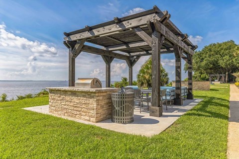 a picnic area with a grill and a pergola overlooking the water