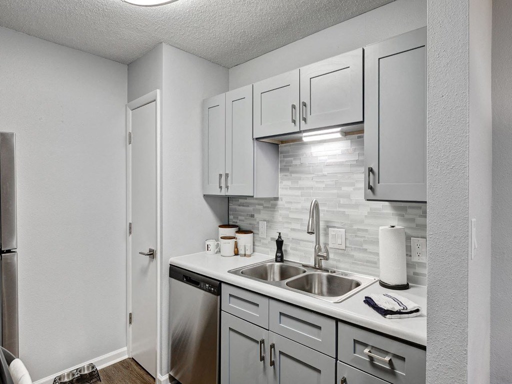 an empty kitchen with white cabinets and a stainless steel sink at The Emory, Pensacola