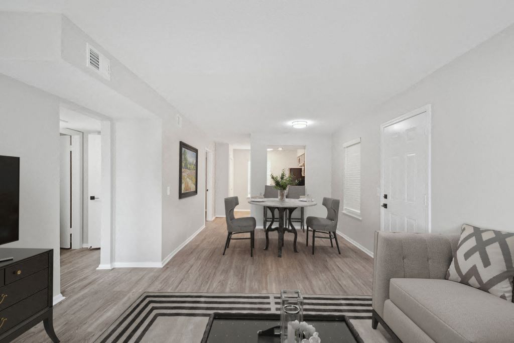 A living room with a grey couch, a coffee table, and a dining table set up in the background.