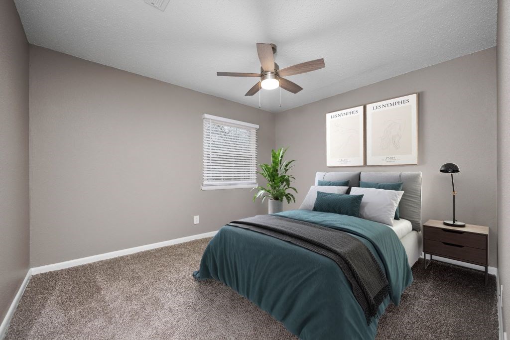 A bedroom with a bed, nightstand, and a plant.