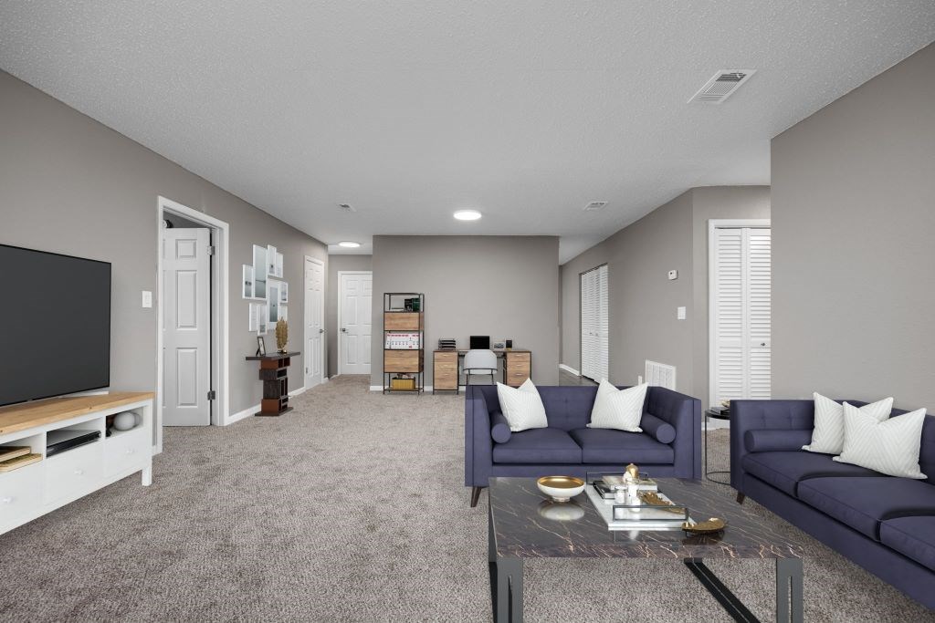 A living room with a grey carpet and a glass coffee table.