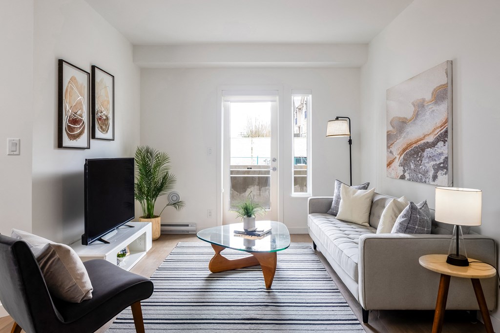 A living room with a grey couch, a black chair, a glass coffee table, and a television.