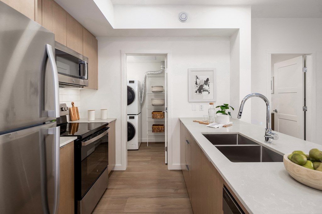 A modern kitchen with a refrigerator, oven, and a bowl of fruit on the counter.