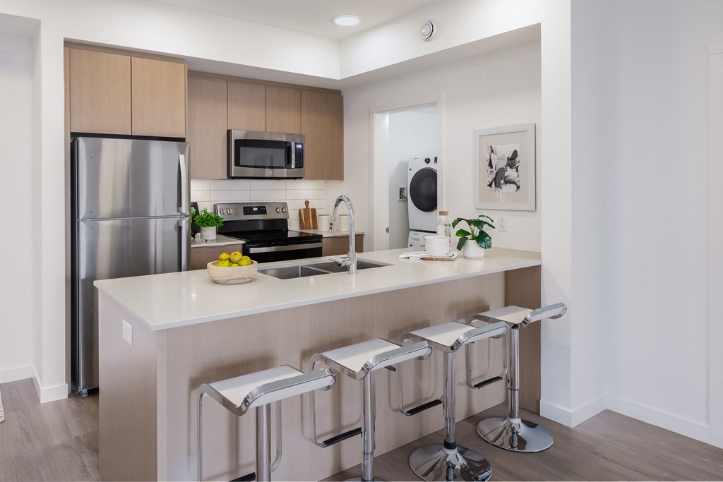 A modern kitchen with a refrigerator, microwave, oven, and a counter with three bar stools.