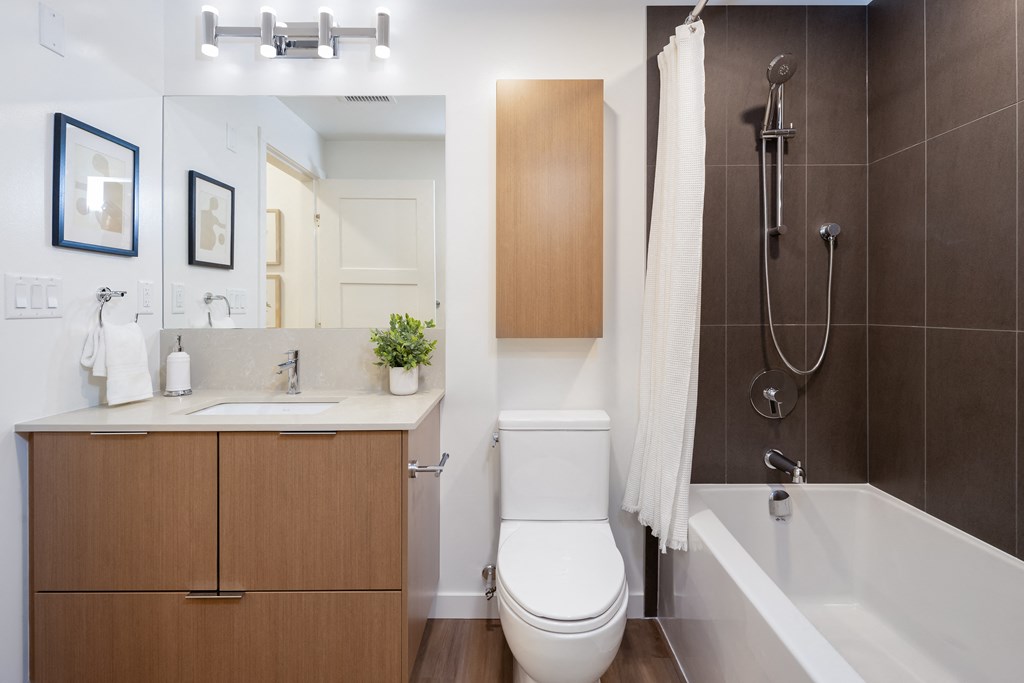 A modern bathroom with a white toilet, a wooden cabinet, and a white bathtub.