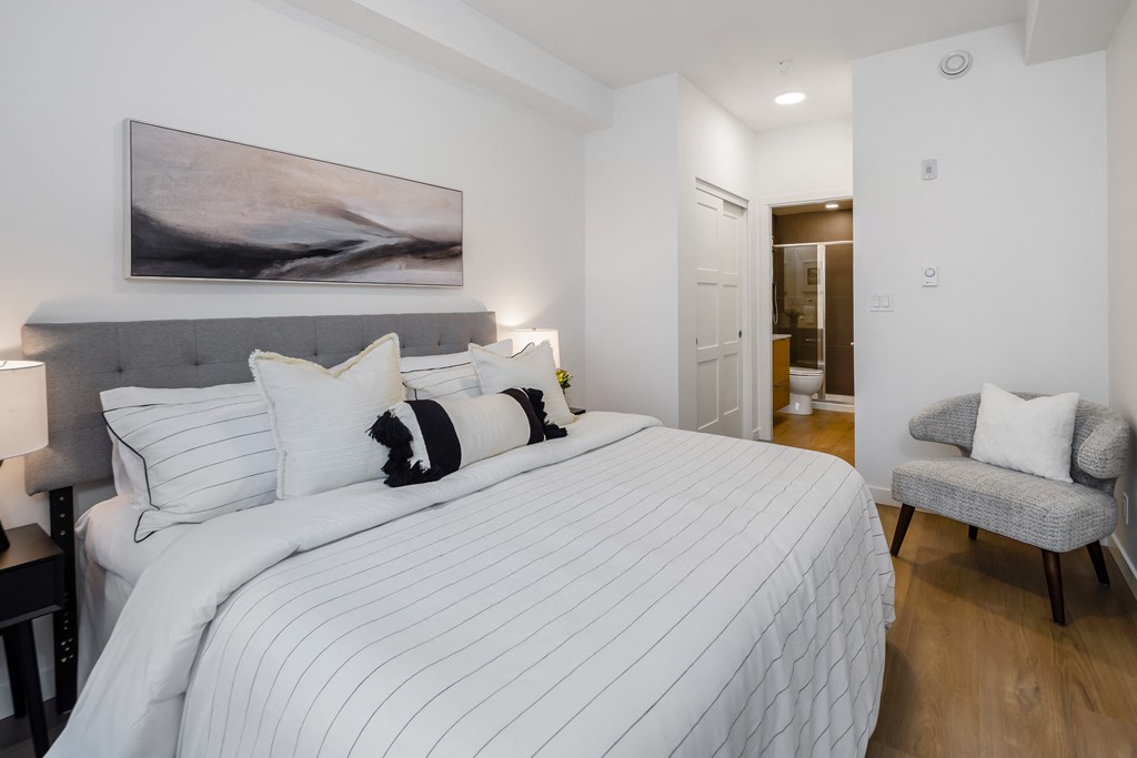 A bedroom with a large bed and a grey armchair.