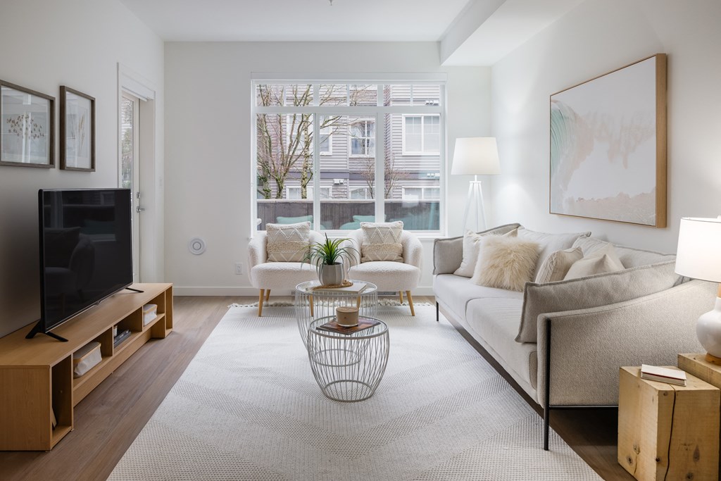 A living room with a grey couch, a television, and a large window.