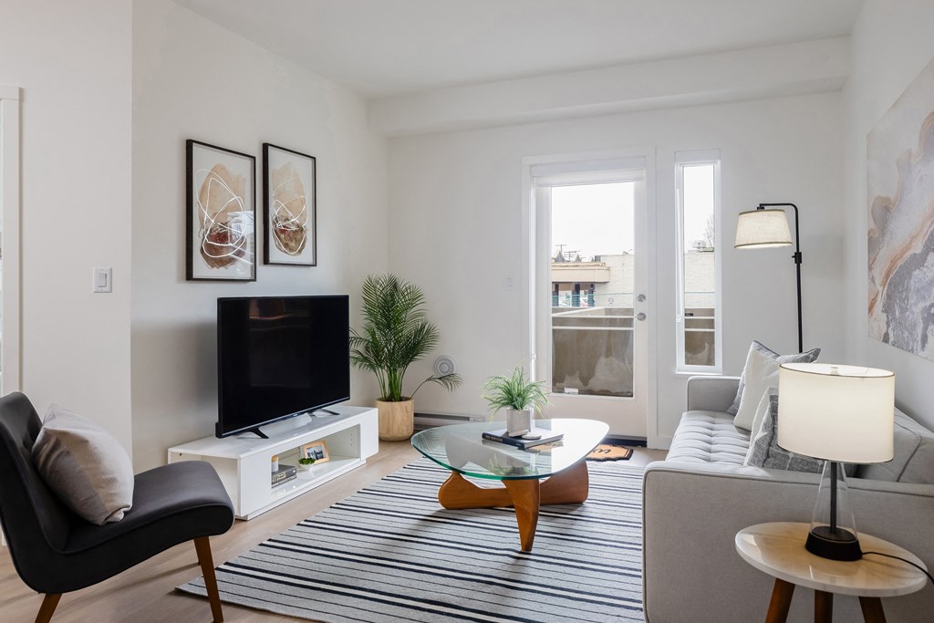 A living room with a black chair, a black television, a glass coffee table, and a striped rug.