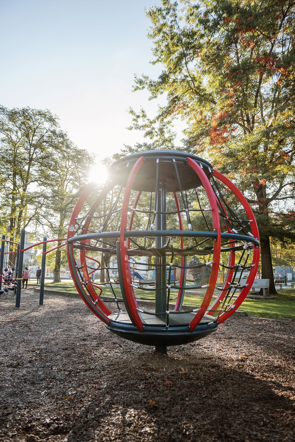 A red and grey spherical playground structure in the middle of a park.